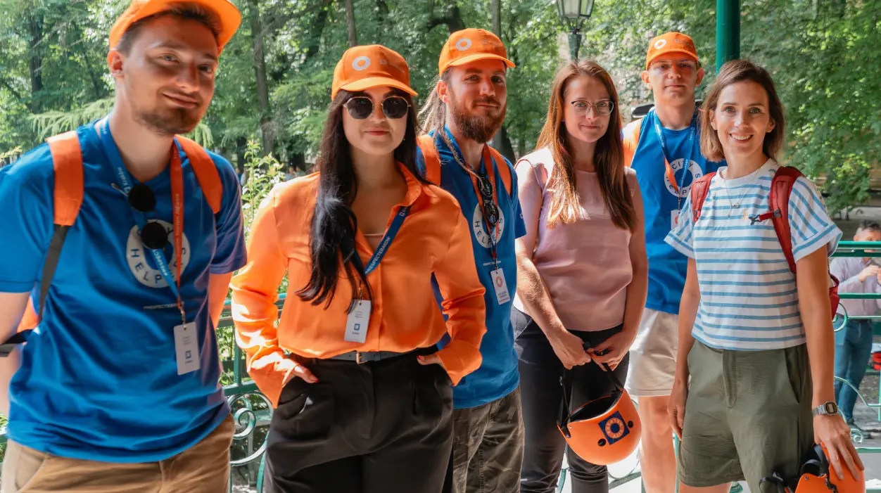Gruppe von City Helpers in Krakau mit orangefarbenen Kappen und blauen T-Shirts, die gemeinsam mit Teammitgliedern von Vasco Electronics für ein Foto posieren.