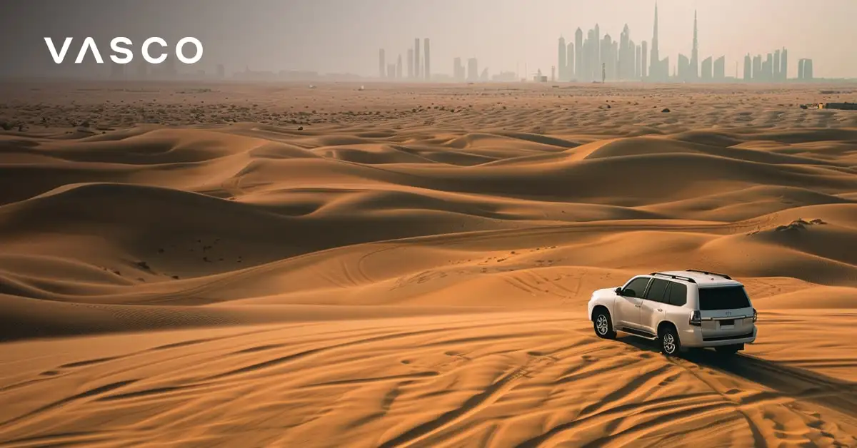 Ein Geländewagen fährt durch die Wüste von Dubai mit der Skyline der Stadt in der Ferne.