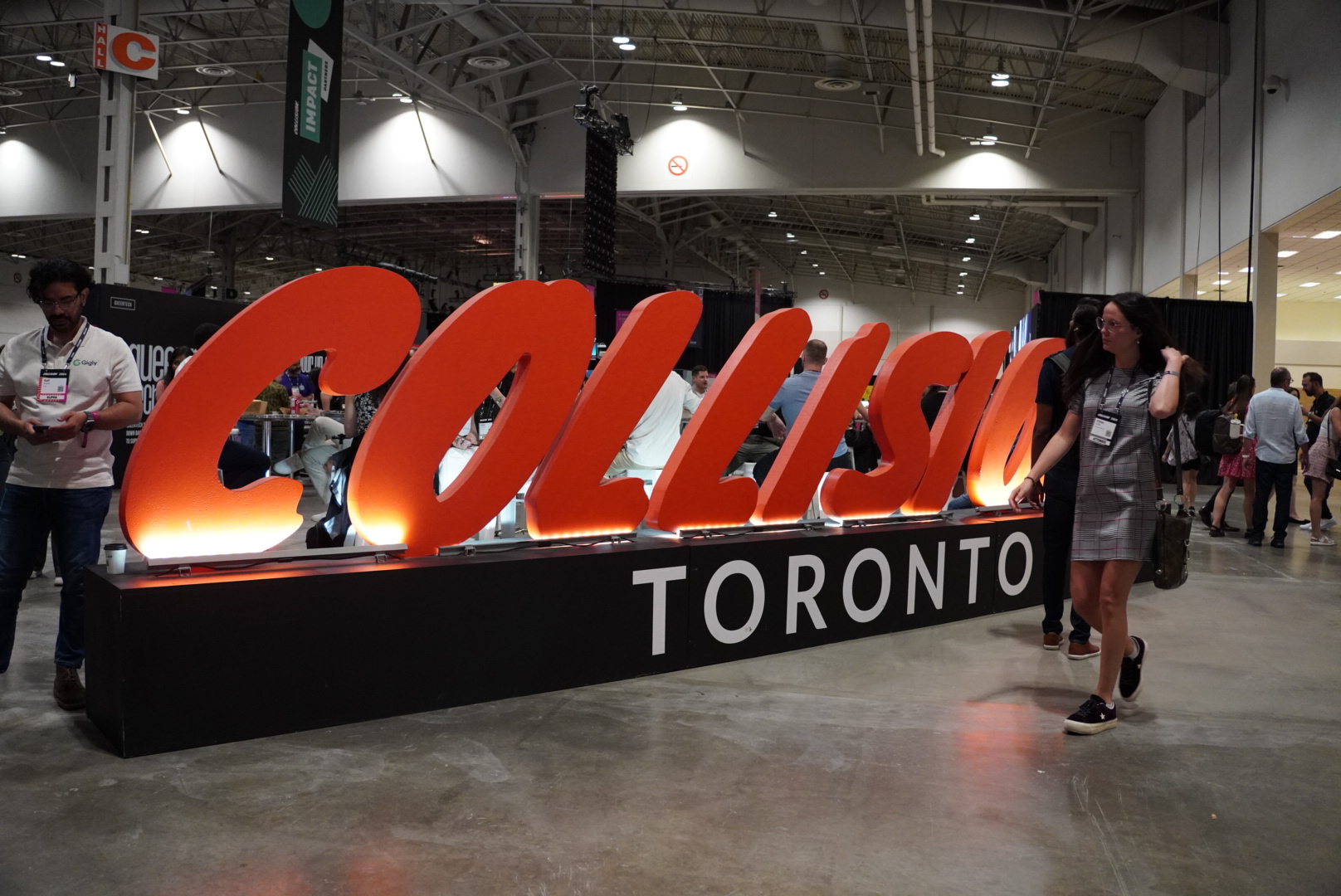 Teilnehmer der Collision-Konferenz in Toronto neben dem großen beleuchteten ‚Collision Toronto‘-Schriftzug in der Messehalle