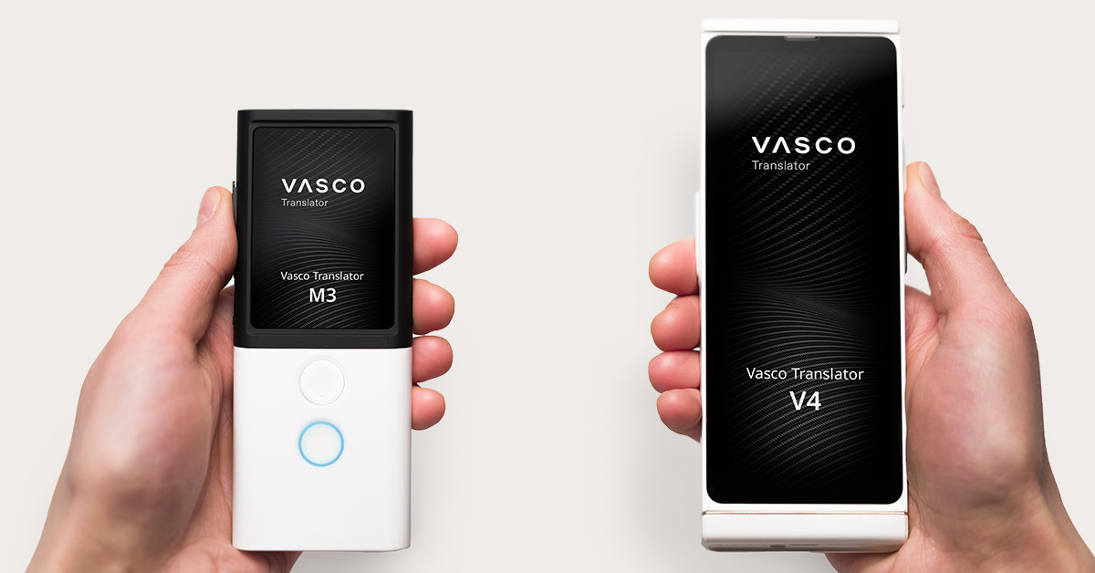 Zwei Hände halten elektronische Übersetzungsgeräte von Vasco – links das Modell M3, rechts das Modell V4. Beide Displays zeigen die Gerätenamen an.