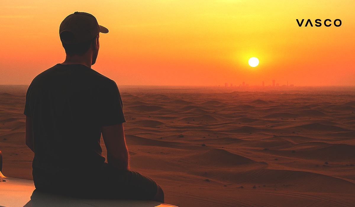 Ein Mann sitzt in einem arabischen Land in einer Wüste und schaut im Sonnenuntergang auf eine Stadt am Horizont