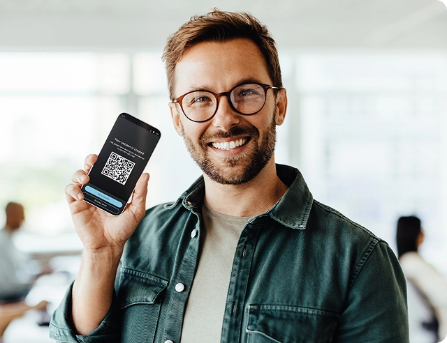 Ein lächelnder Mann hält ein Smartphone in der Hand, auf dem ein QR-Code für die Anmeldung bei Vasco Audience angezeigt wird.