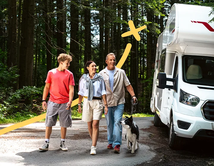Eine dreiköpfige Familie – zwei Eltern und ein Kind – mit Hund verlässt an einem sonnigen Tag ihren geparkten Wohnmobil. Sie lächeln, unterhalten sich und genießen die gemeinsame Zeit.