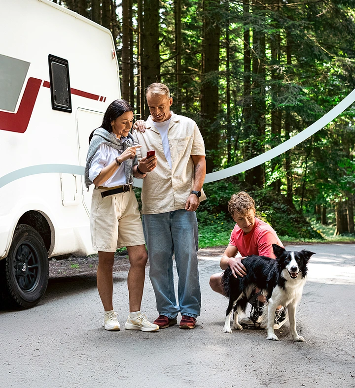 Zwei Erwachsene stehen neben einem Wohnmobil und schauen auf einen Vasco Translator V4. Neben ihnen streichelt ihr Sohn einen Hund und fängt so eine friedliche Familienreise ein.