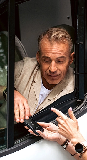Ein Mann sitzt in einem Auto und spricht in den Vasco Translator Q1, den ihm jemand hinhält.
