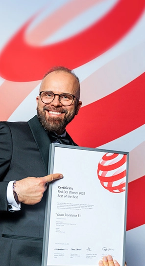 Der Geschäftsführer von Vasco Electronics zeigt lächelnd auf eine Urkunde für den Red Dot Design Award, die er in der Hand hält.