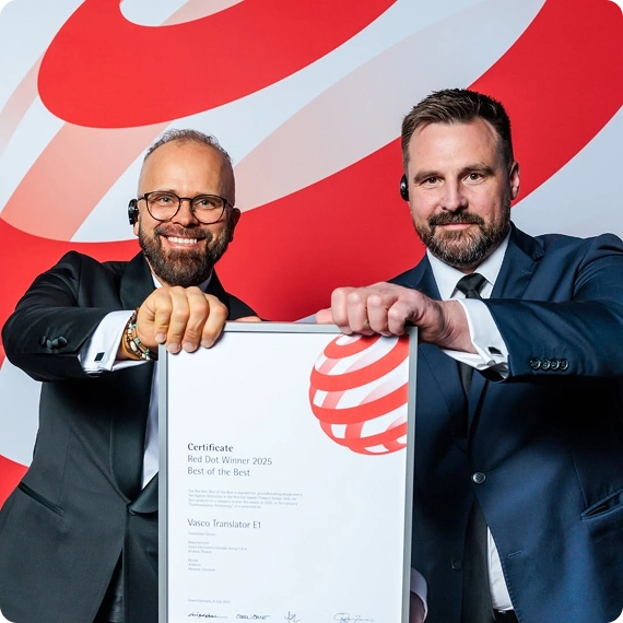 Two men in formal business attire—the left in a tuxedo with glasses, the right in a dark blue suit—jointly holding a framed award certificate with both hands. The certificate explicitly reads 