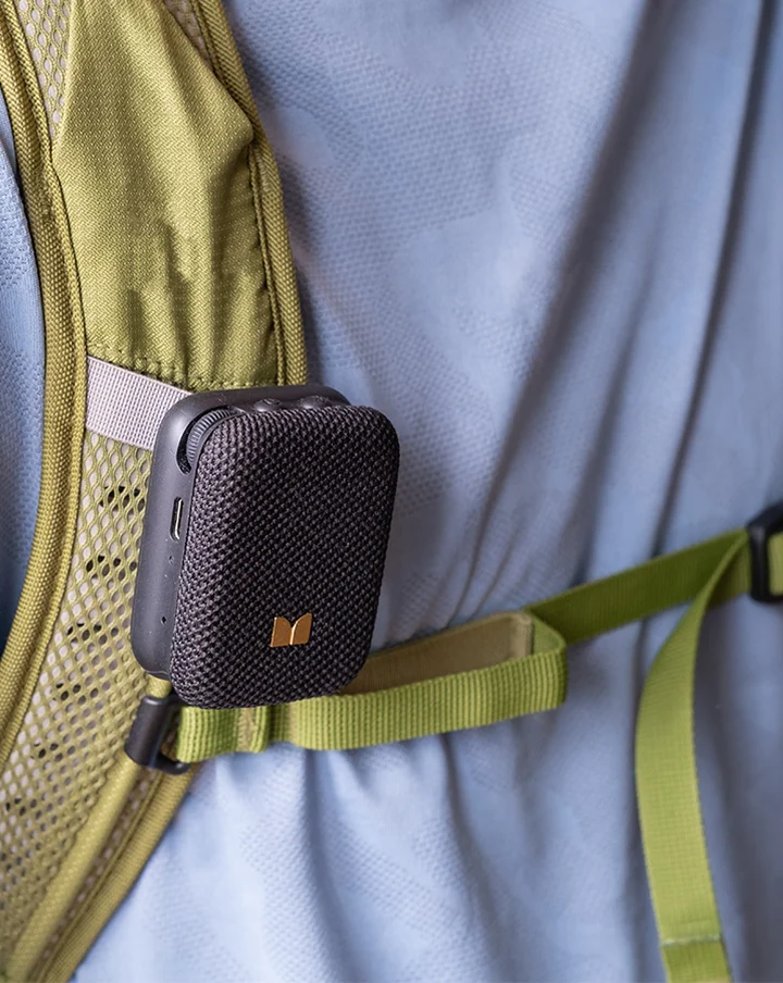 Schwarzer Mini-Bluetooth-Lautsprecher, befestigt am olivgrünen Gurt eines Rucksacks